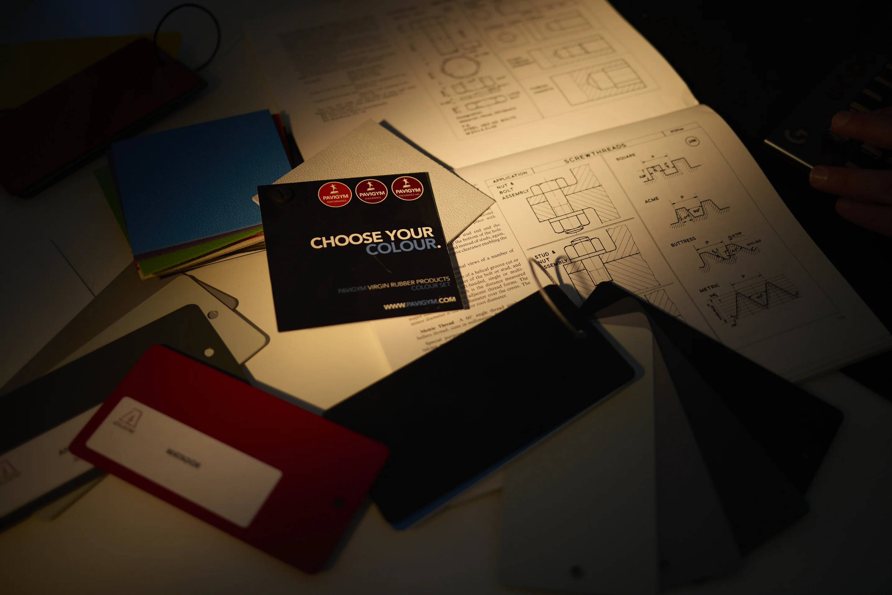 Color swatches and a card reading 'CHOOSE YOUR COLOUR' resting on engineering diagrams with screw thread drawings.