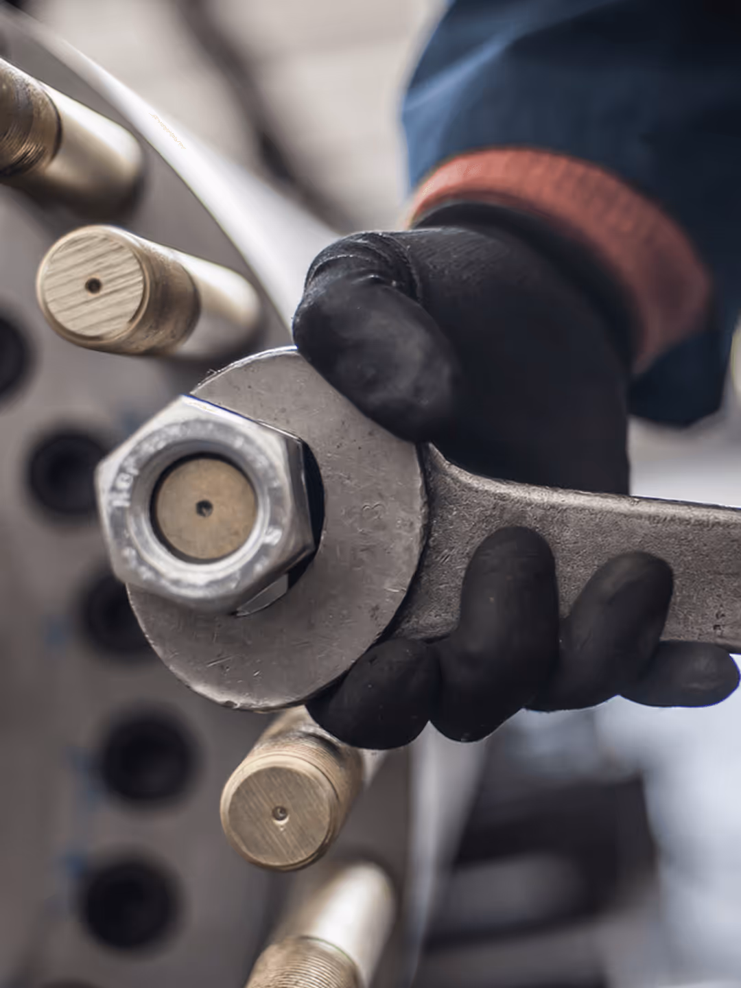 Hand trägt Handschuh und hält Schraubenschlüssel, zieht große Sechskantschraube an Metallkonstruktion fest.