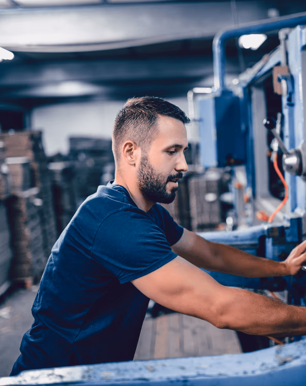 Mann bedient eine große, blaue Industrieanlage in einer Fabrikumgebung.