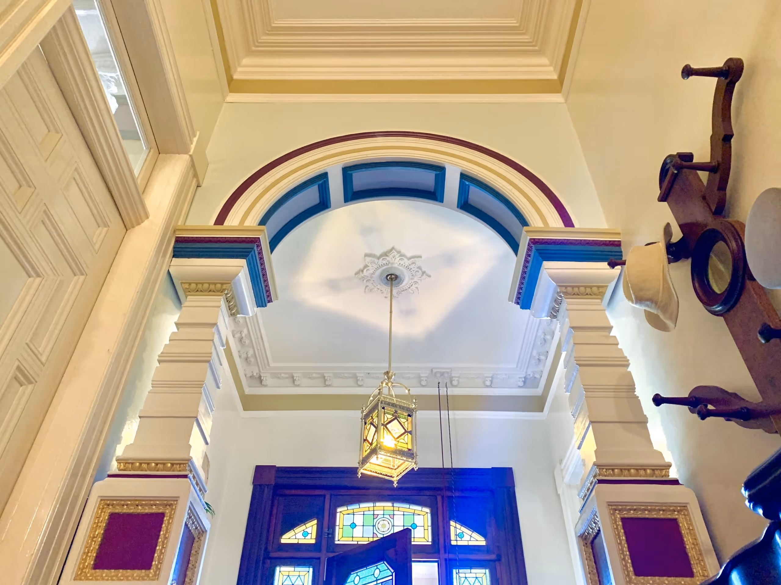 Ornate hallway ceiling with an arched doorway, decorative columns, stained glass window, and a hanging lantern light fixture.