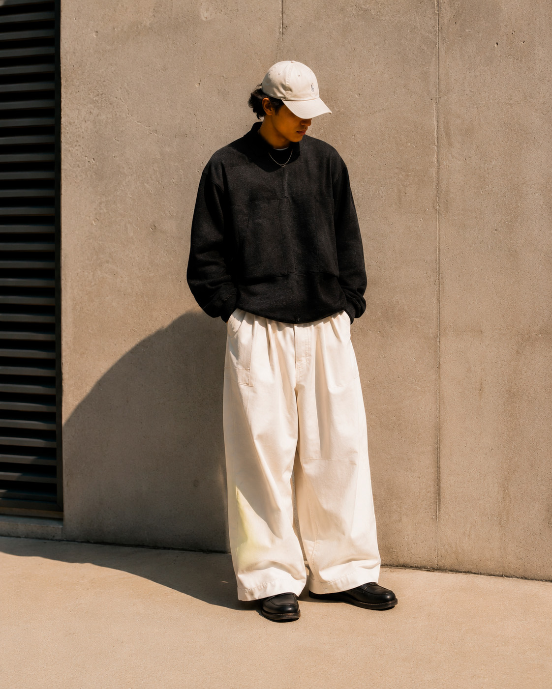 Modern streetwear outfit with a black sweatshirt, cream cap, wide white trousers, and black leather shoes.