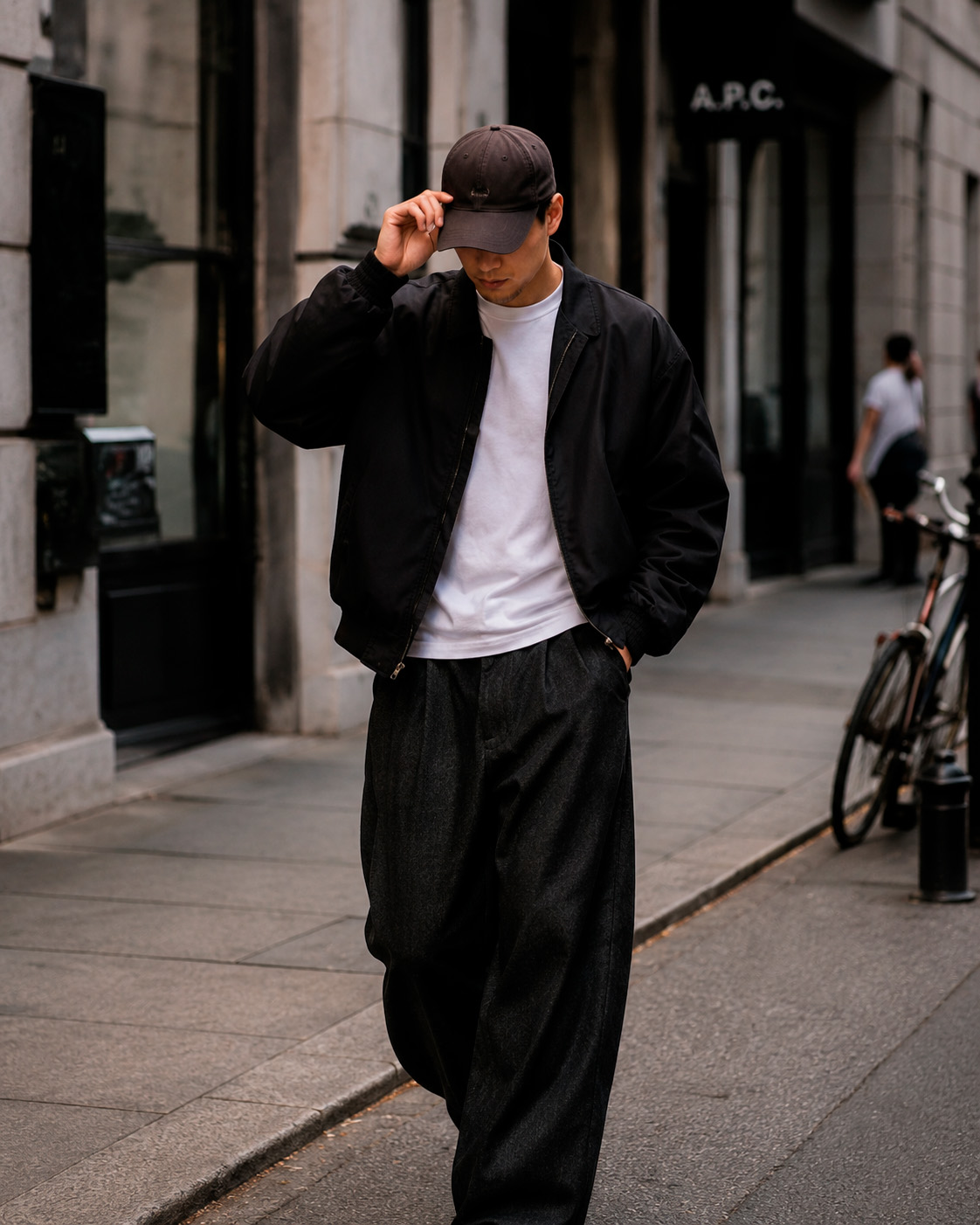 Balanced streetwear outfit with a black jacket, white T-shirt, cap, wide dark trousers, and black shoes.