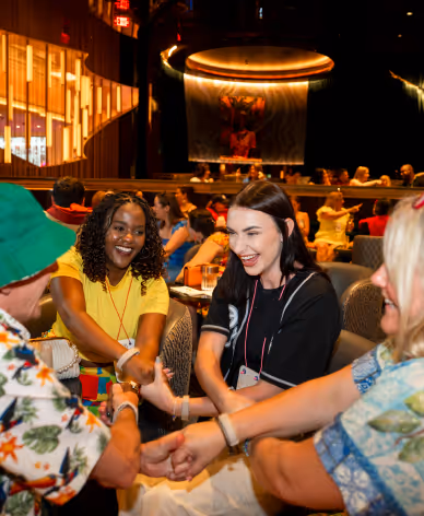 Group of diverse young adults holding hands and smiling in a lively, warmly lit social setting.