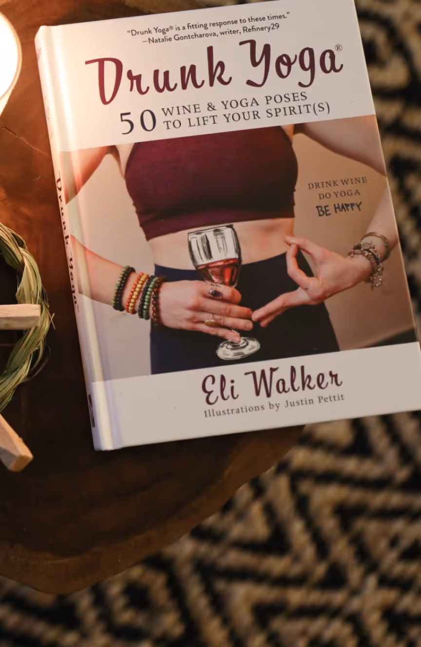 Book titled 'Drunk Yoga: 50 Wine & Yoga Poses to Lift Your Spirit(s)' by Eli Walker, showing a person holding a glass of wine in a yoga pose.