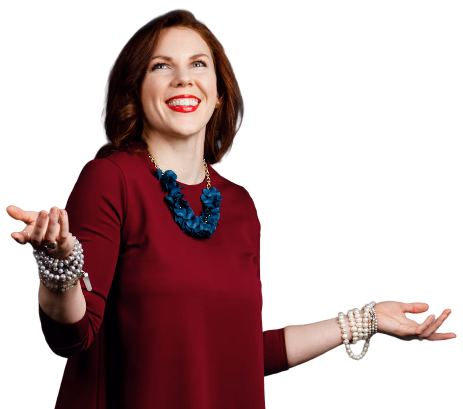 Smiling woman with red lipstick wearing a burgundy top, blue statement necklace, and multiple pearl bracelets on both arms against a transparent background.