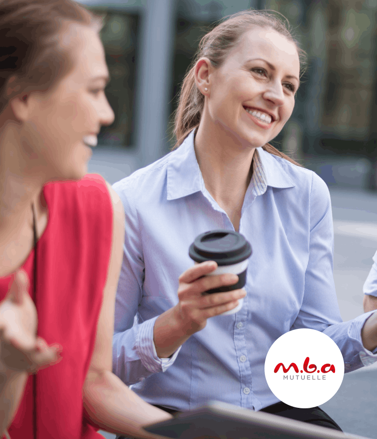 Deux femmes souriantes discutent à l'extérieur, l'une tenant un gobelet de café à emporter.