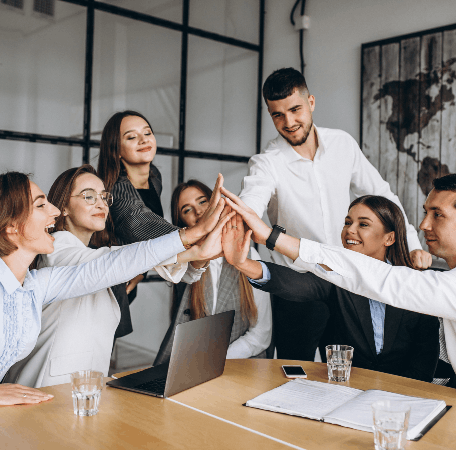 Groupe de jeunes professionnels souriants réunis autour d'une table, effectuant un high-five collectif dans un bureau moderne.