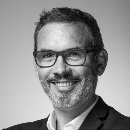 Portrait en noir et blanc d'un homme souriant portant des lunettes et un costume.