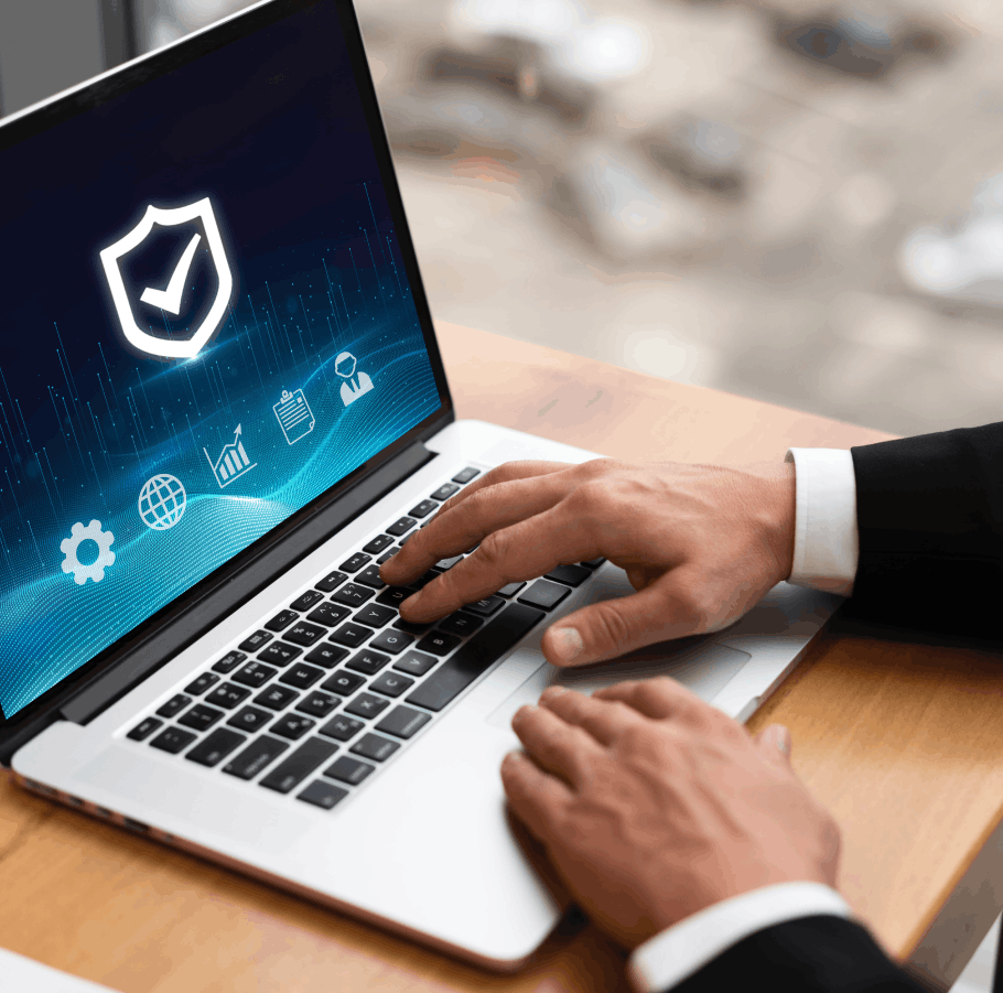 Mains d'un homme en costume utilisant un ordinateur portable affichant une icône de bouclier avec une coche, symbolisant la sécurité informatique.