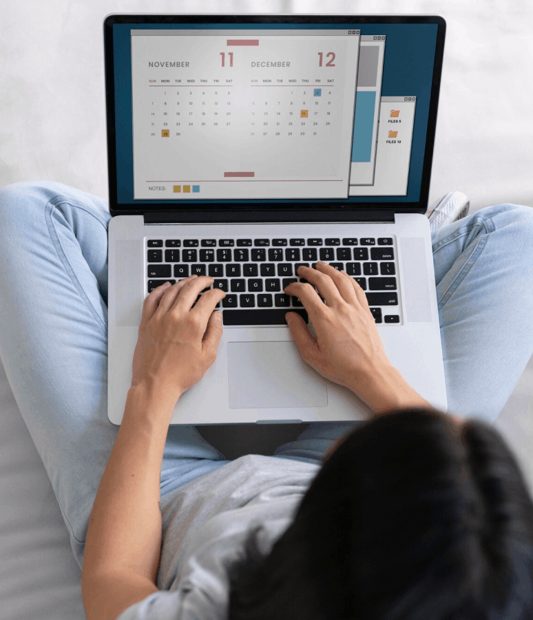 Person assise en tailleur utilisant un ordinateur portable affichant un calendrier des mois de novembre et décembre sur l'écran.