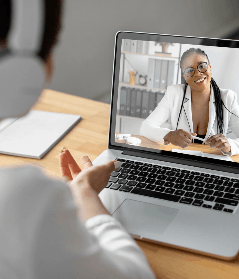Personne portant un casque utilisant un ordinateur portable pour une visioconférence avec une femme souriante en veste blanche à l'écran.
