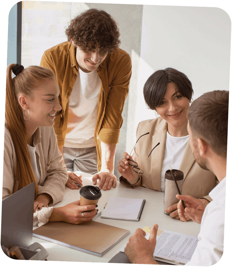 Quatre personnes discutent et sourient autour d'une table avec des cahiers, un ordinateur portable et des tasses de café.