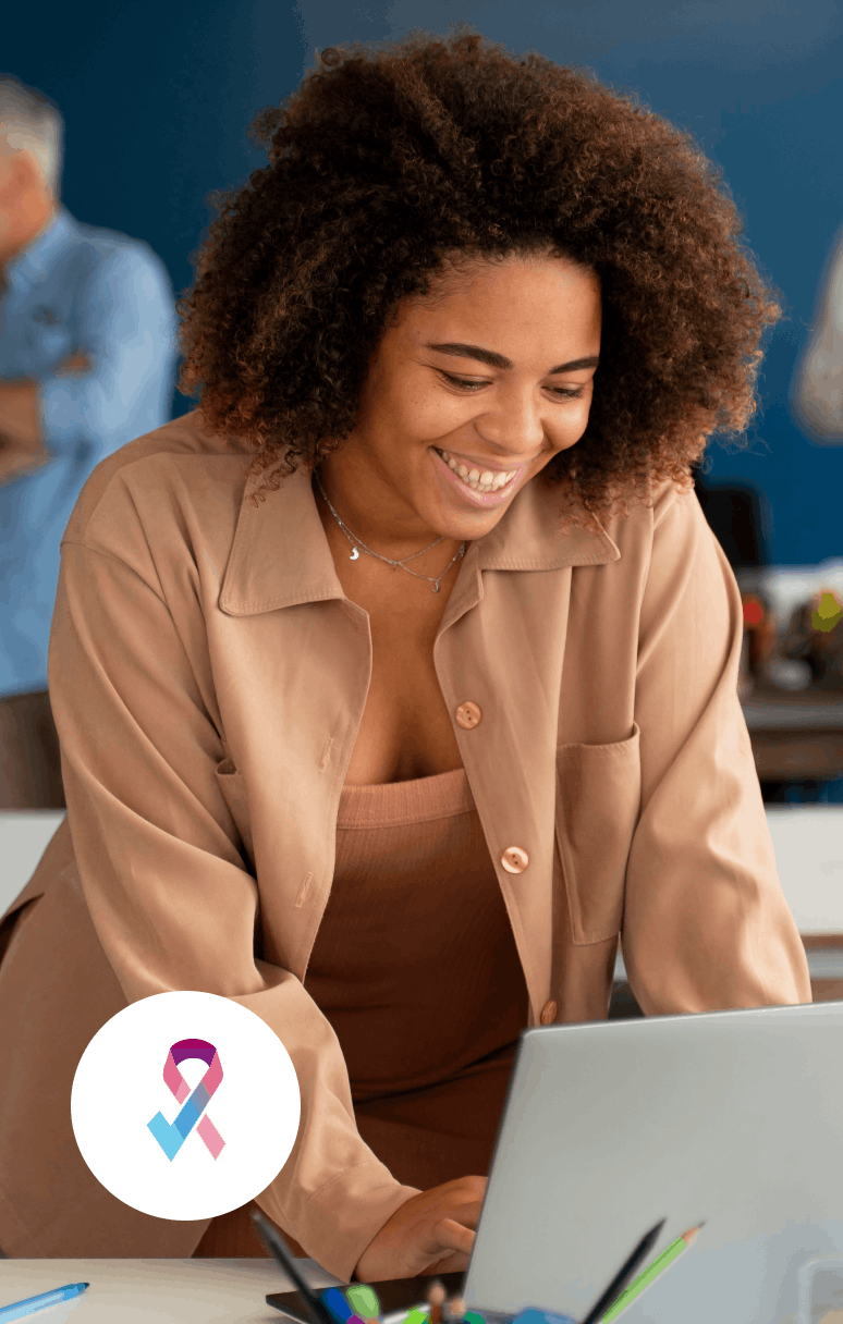Femme souriante regardant un ordinateur portable dans un bureau, avec un ruban rose et bleu symbolique en bas à gauche.