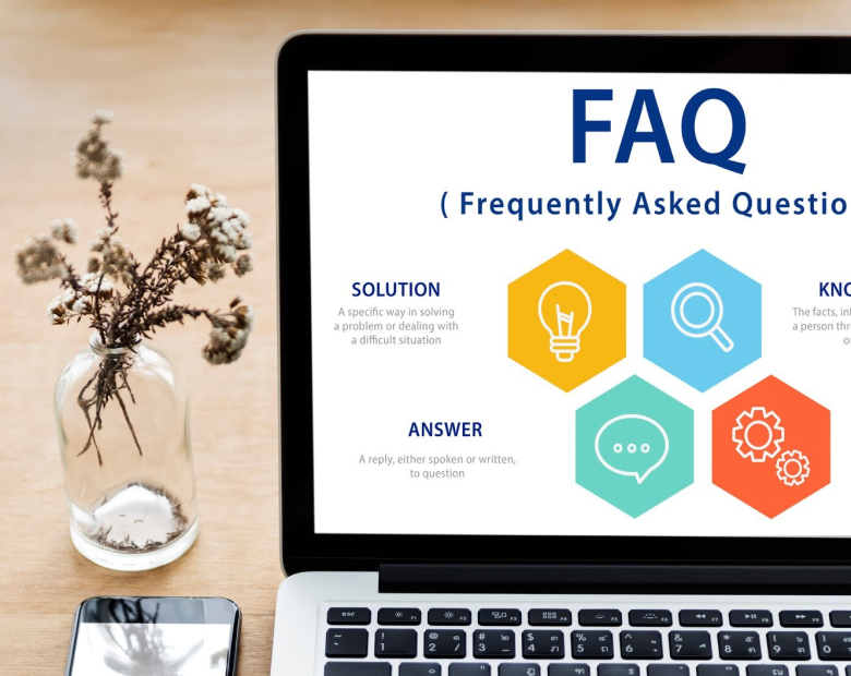 Ordinateur portable affichant une page FAQ avec des définitions pour solution, réponse et connaissance, à côté d'un vase en verre avec des fleurs séchées et un téléphone sur un bureau en bois.