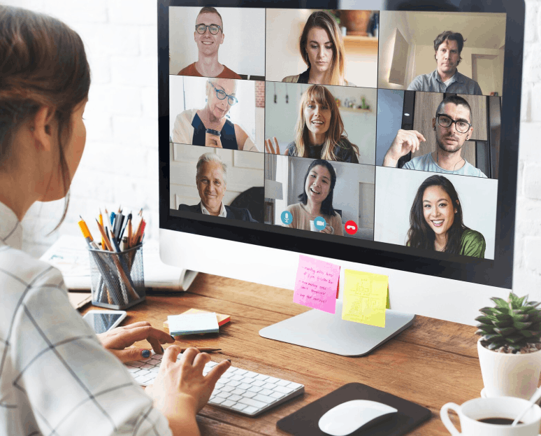 Personne travaillant à un bureau avec un ordinateur affichant une réunion vidéo avec huit participants sur l'écran.
