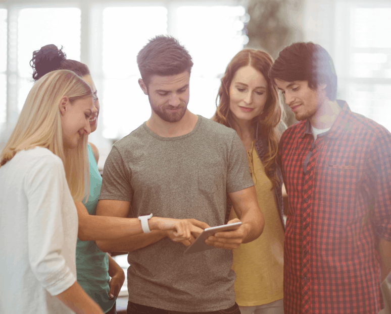 Un groupe de cinq jeunes adultes regardant ensemble un écran de tablette dans une pièce lumineuse.