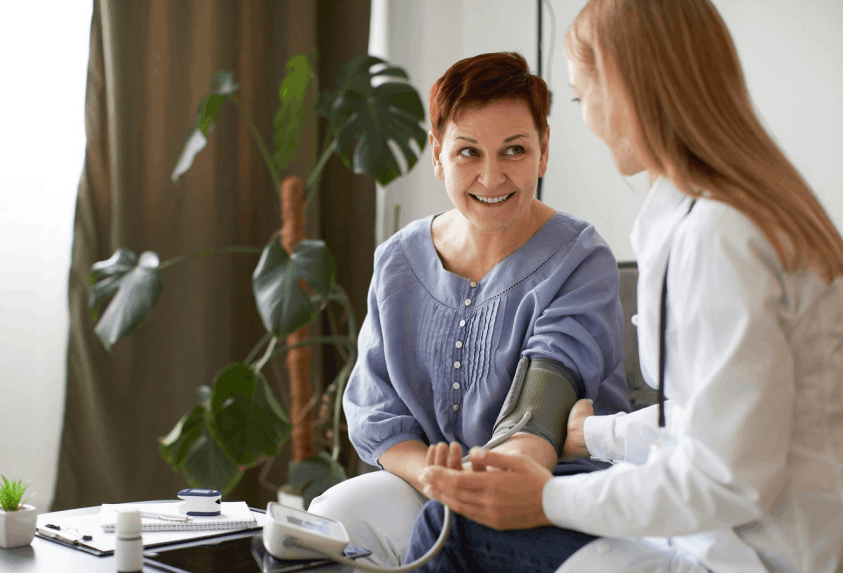Une patiente souriante porte un brassard de tensiomètre pendant qu'un médecin prend sa tension artérielle dans un cabinet médical.