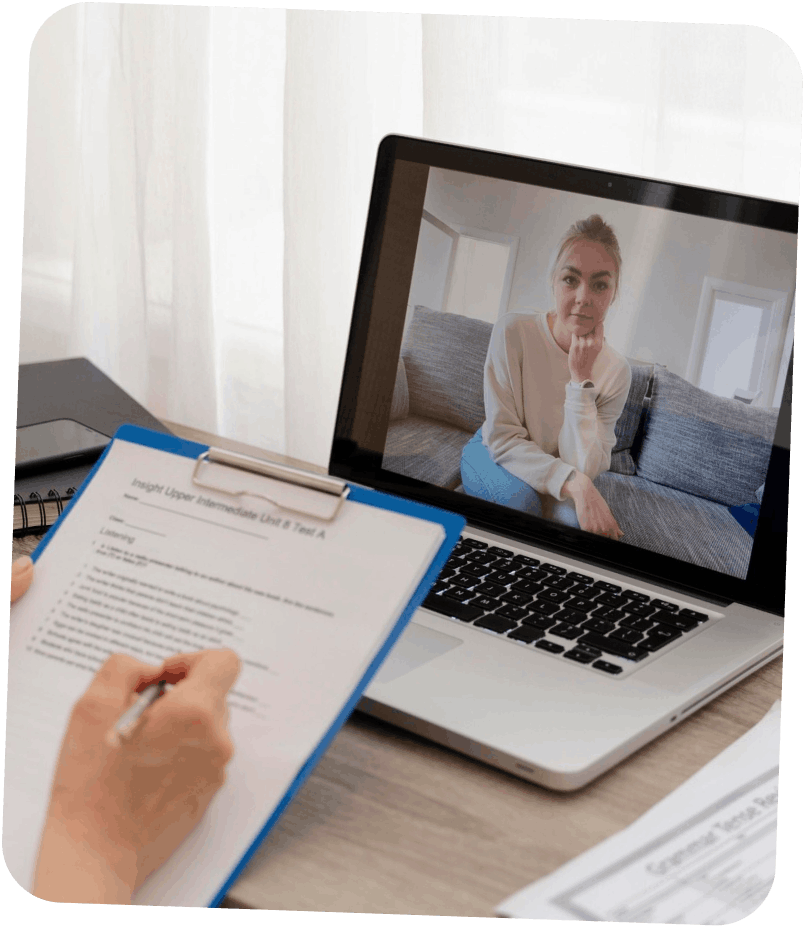 Personne prenant des notes sur une feuille avec un stylo, en visioconférence avec une femme assise sur un canapé visible sur l'écran d'un ordinateur portable.