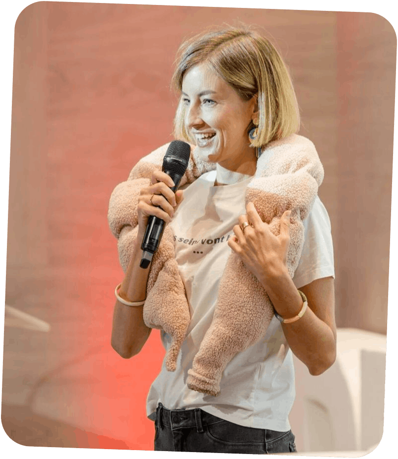 Dr Charlotte Berthaut avec un micro, portant une veste en moumoute beige sur les épaules.