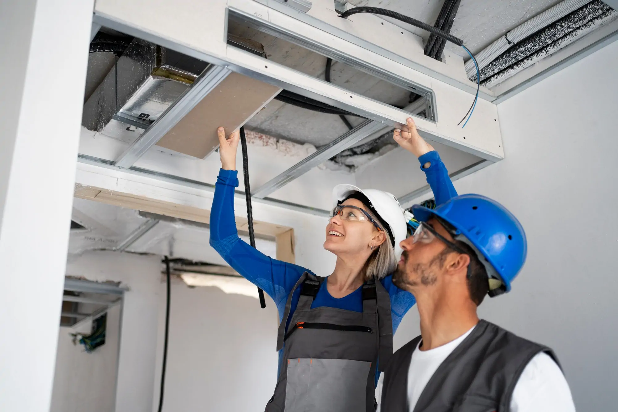 Two workers installing ceiling duct panels.