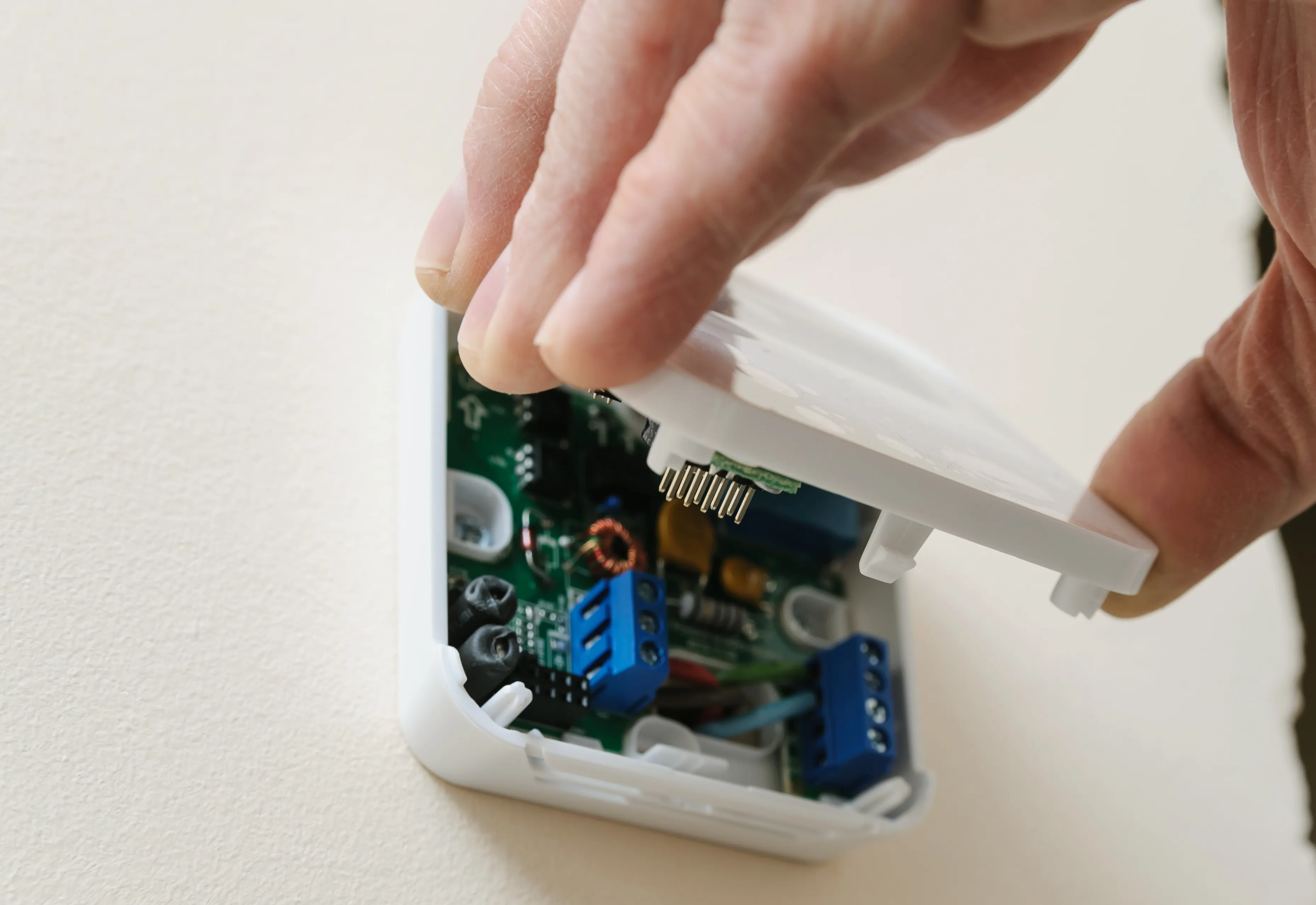 Hand opening a white wall-mounted thermostat to reveal circuit board and wiring for installation