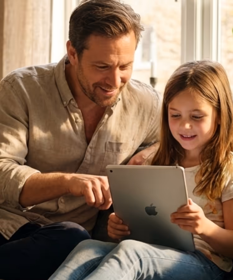 Father and daughter sitting together, engaging with an Apple iPad.