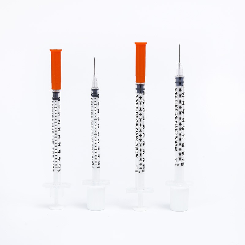 Four insulin syringes with orange caps, ready for injection. Medical supplies.