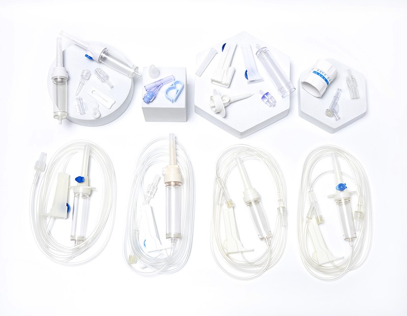 Medical IV drip sets and components arranged on white platforms and against a white surface, showcasing medical equipment.