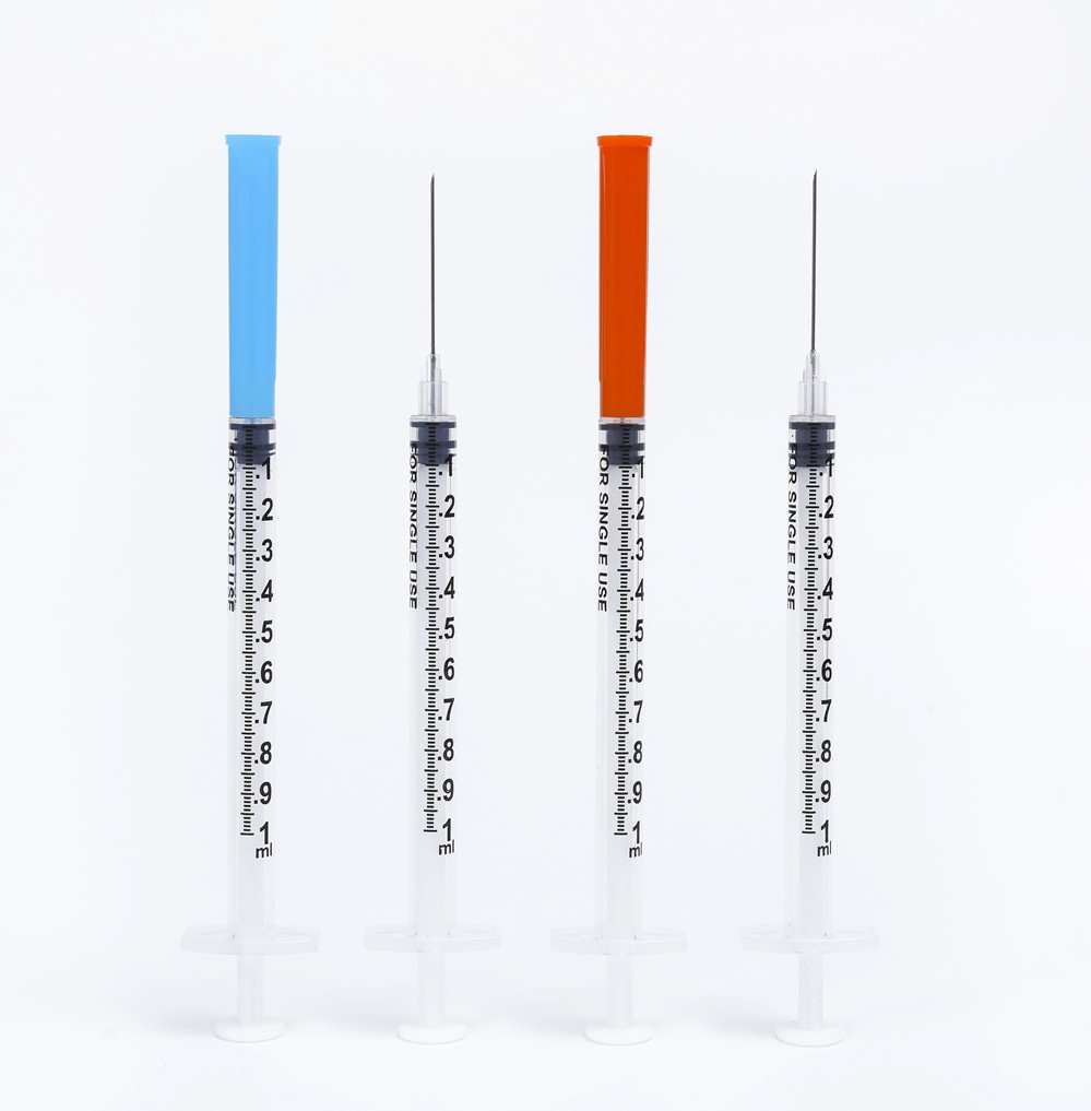 Four syringes with needle tips, blue and orange caps, ready for medical use and injections.