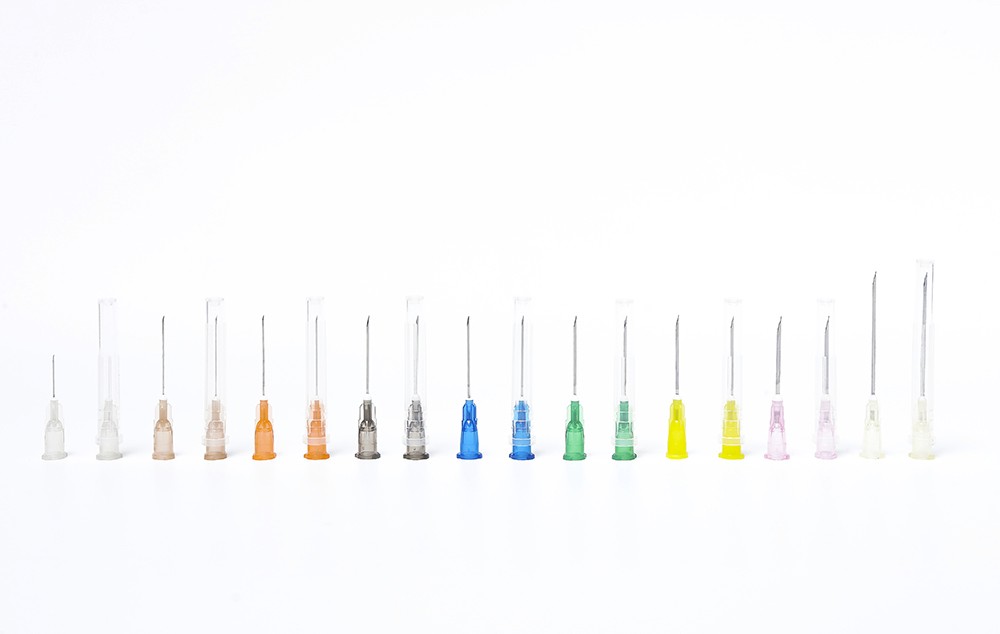 A line of various medical needles with different colored bases. Needles shown on a white background.
