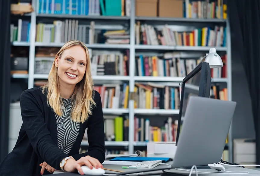 Seven industrial workers wearing orange safety jackets and white helmets standing outdoors in front of metal shelving under a blue sky.