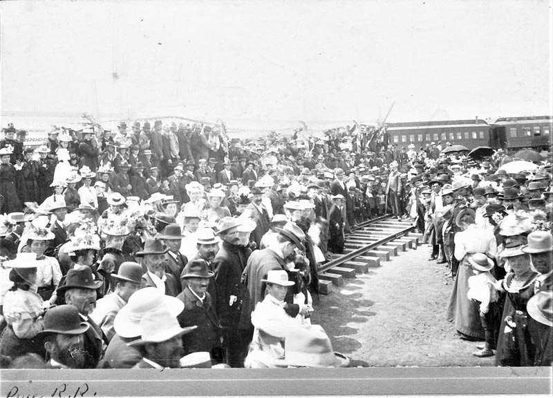 Weiser, May 19, 1899. A crowd gathers around Thomas Bates who stands on the newly-laid railroad ties with a spike-driving hammer in his hands as he is about to drive the first spike of the Pacific & Idaho Northern Railway line.
