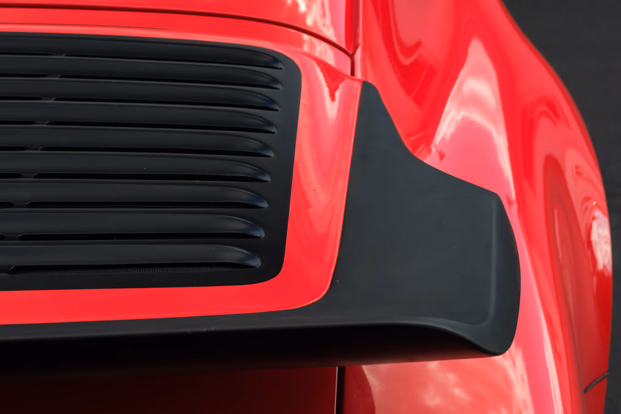 Close-up of a red car's rear vent grille with black aerodynamic trim.