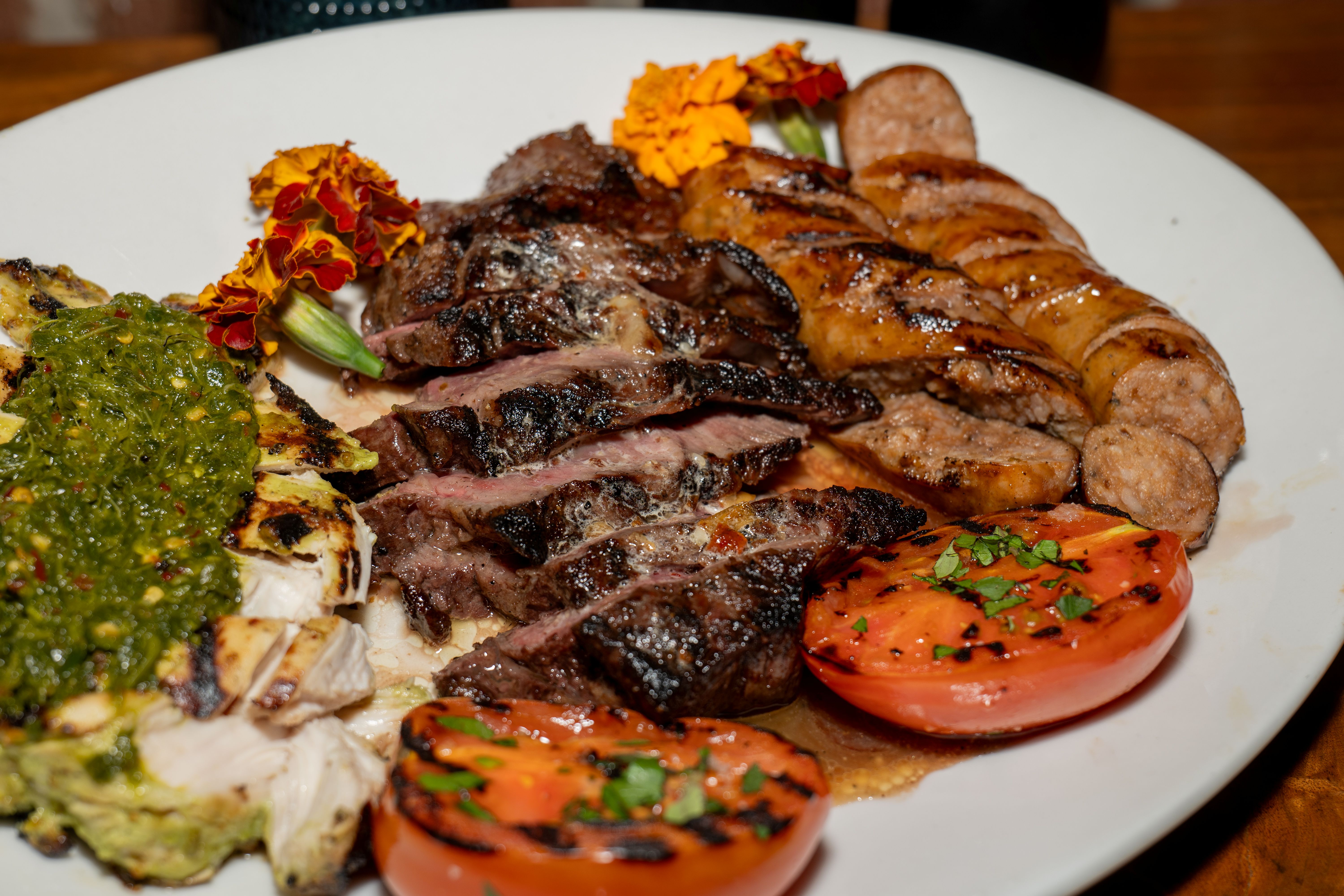 Plate with a pulled chicken sandwich on toasted bread and a side of crispy seasoned fries on a wooden table with blurred warm lights in the background.