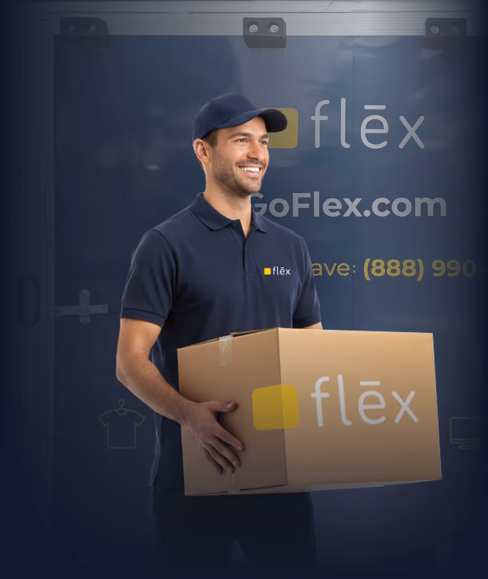 Smiling Flex team member in navy polo and cap holding a large cardboard box labeled "flëx" in front of a dark blue branded trailer door.