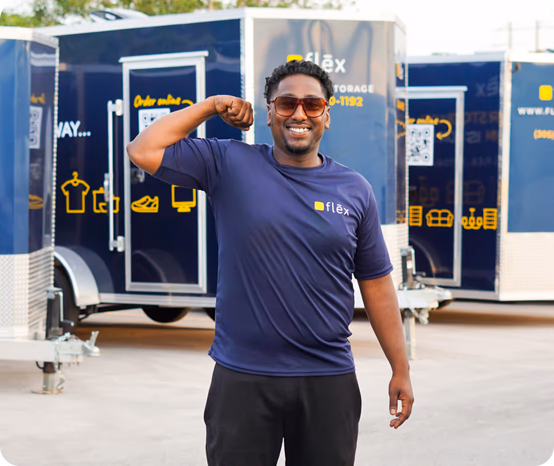 Man flexing his bicep and smiling confidently in front of multiple navy & yellow Flex storage trailers outdoors.