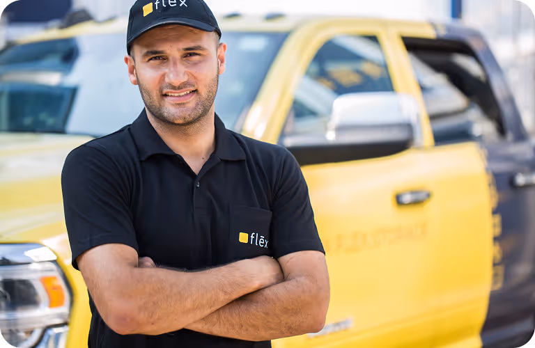 Flex worker in branded cap and polo standing in front of ram truck branded with Flex colors yellow and navy.