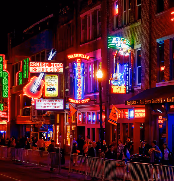 Night street scene in Nashville with neon signs for Ernest Tubb Record Shop, Nashville Crossroads, and AJ's Good Time Bar, with people lined up along the sidewalk.