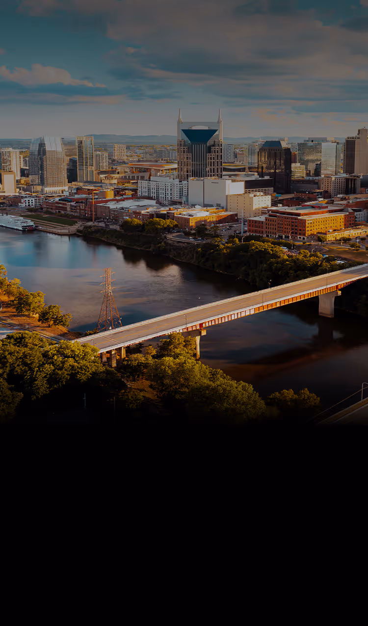 Aerial view of Nashville skyline at sunset featuring the iconic AT&T Building and a bridge over the Cumberland River.