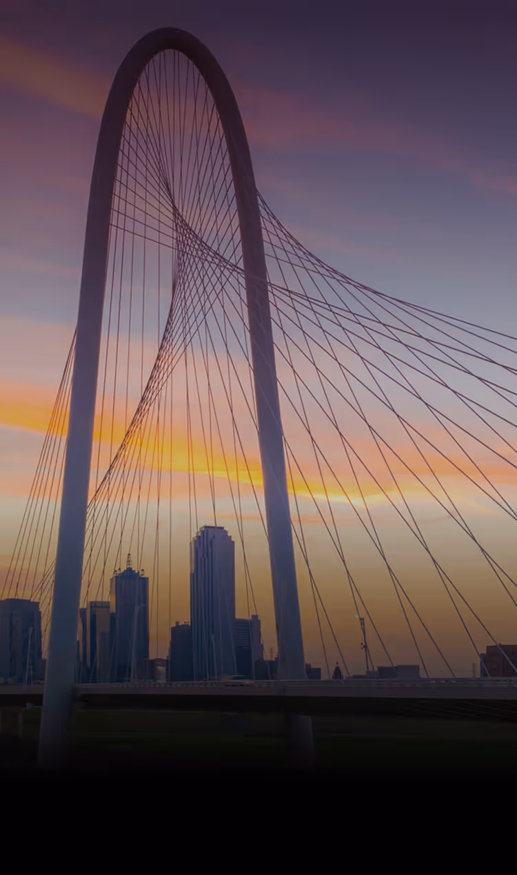 Margaret Hunt Hill Bridge in Dallas at sunset with city skyline in the background.