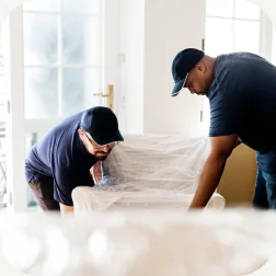 Two movers wrapping furniture in a home