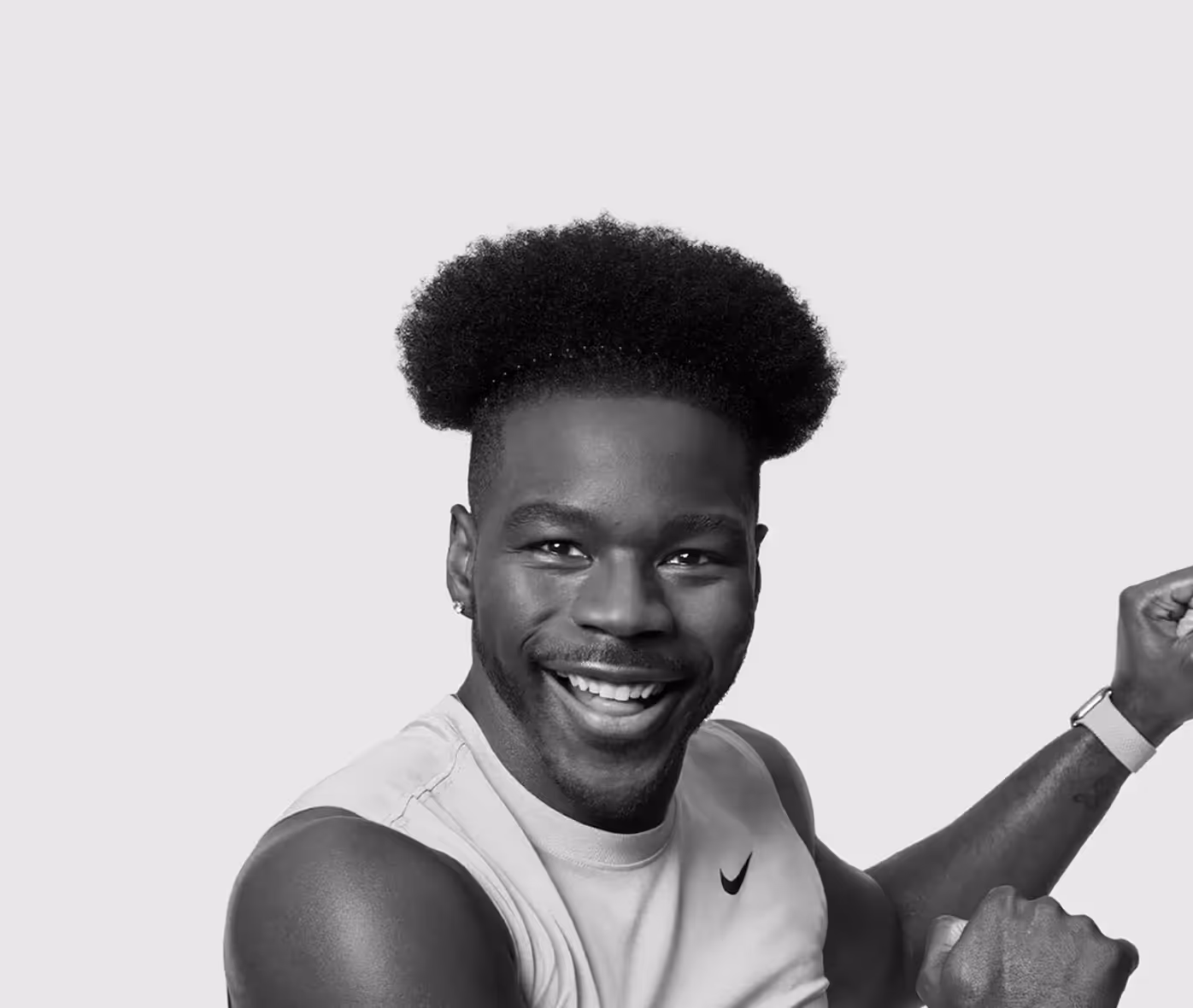 Smiling man with afro hairstyle wearing a sleeveless Nike top and a smartwatch, posing with flexed arms.