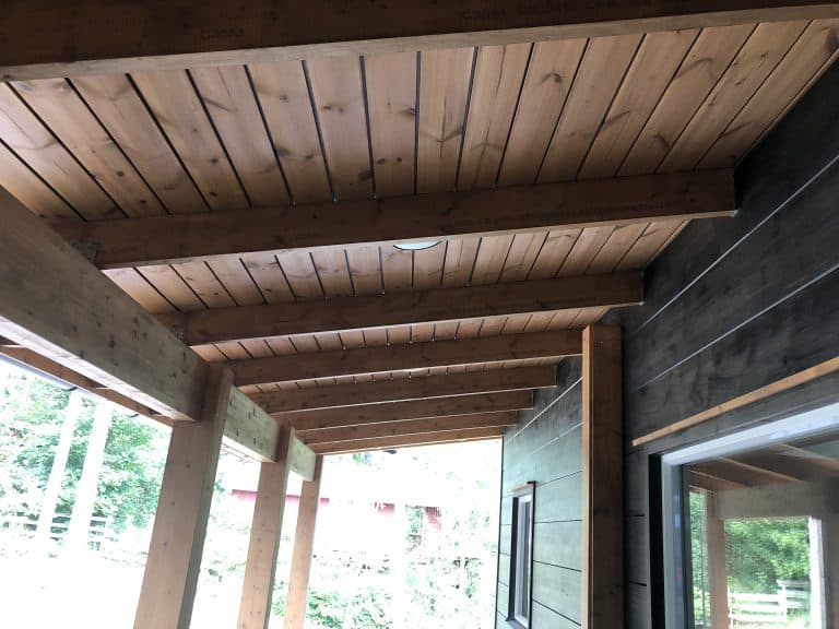 Puurakenteinen katos, jossa on vaaleanruskea puukatto ja tummempi seinä, valaistus on luonnollista.