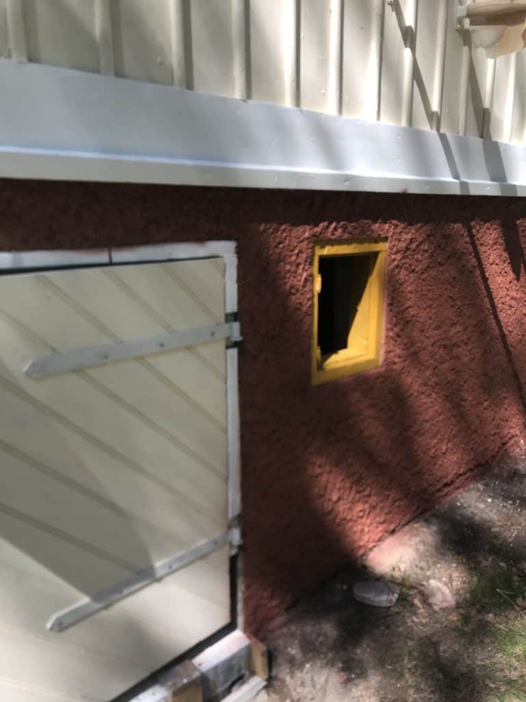 Rakennuksen seinässä on luukku ja pieni keltainen ikkuna, seinä on punaruskea ja valaistus on luonnollinen.