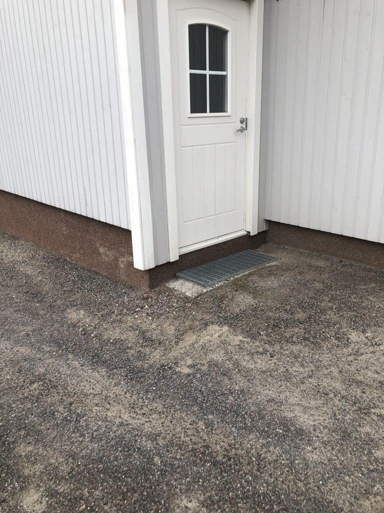 Ulko-ovi valkoisessa rakennuksessa, ruskea sokkeli ja harmaa kivipiha. Valoisa sää.