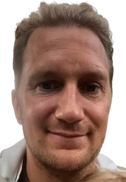 Lähikuva vaaleahiuksisesta miehestä, jolla on siniset silmät ja lyhyt parta, mustalla taustalla.