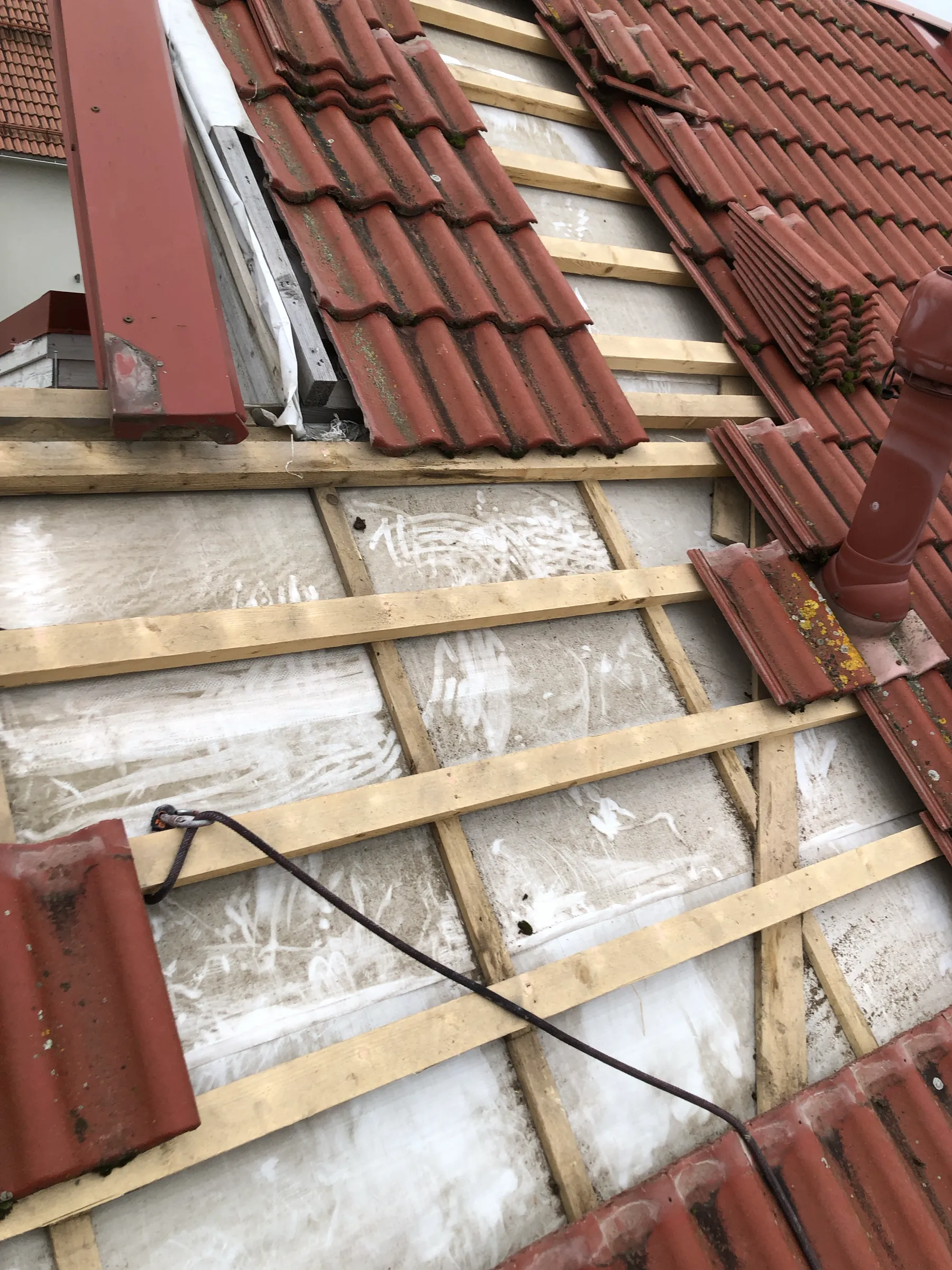 Katto on osittain purettu, paljastaen puurakenteet ja valkoisen aluskatteen. Punaiset tiilet ovat osittain paikoillaan.