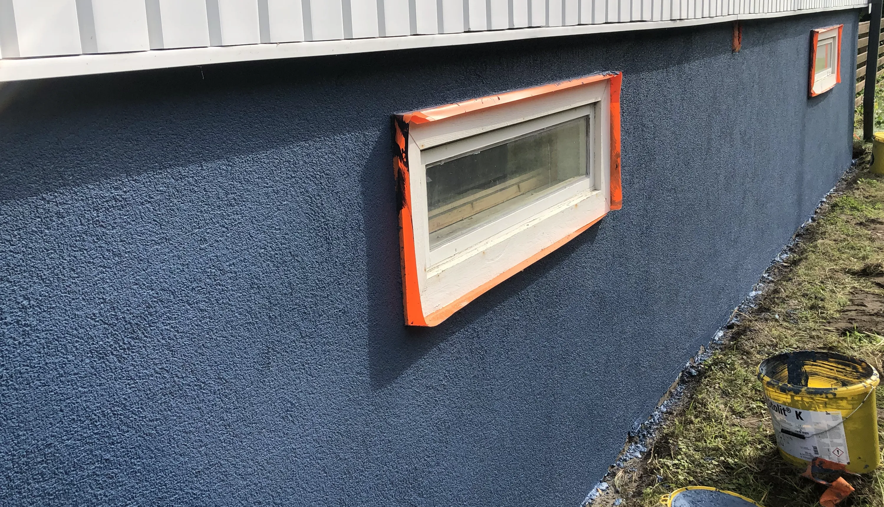 Sininen seinä, jossa on kaksi ikkunaa ja keltainen maalipurkki.