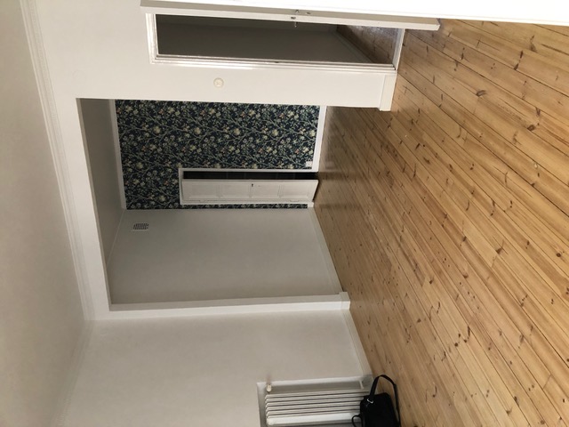 Huoneessa on puulattia, tapetoitu seinä, valkoinen seinä ja valkoinen katto. Huone on valoisa.