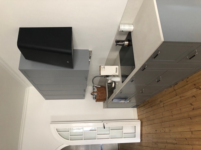 Keittiön sisätiloissa on harmaat kaapit, puulattia, musta liesituuletin ja valkoinen ikkuna.